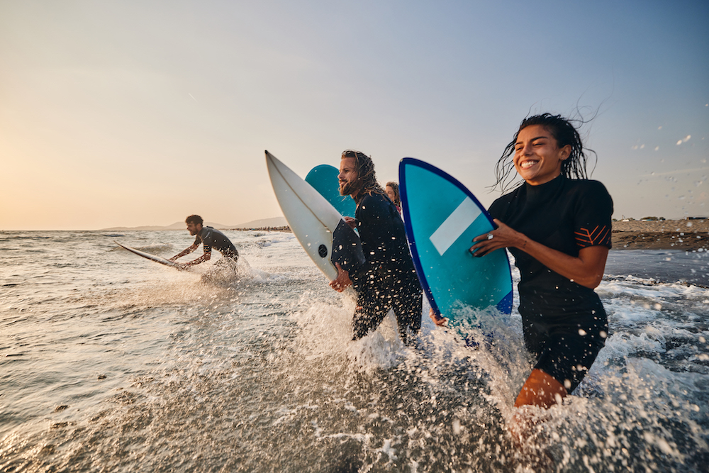 people running into ocean with surfboards 